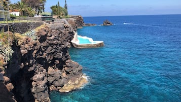 A coastal area with a rocky cliff, clear blue water, and a small pool.