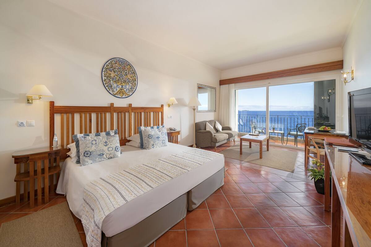 Une chambre d’hôtel comprenant un lit, un bureau, une chaise, une télévision, un balcon avec vue et un élément décoratif mural.