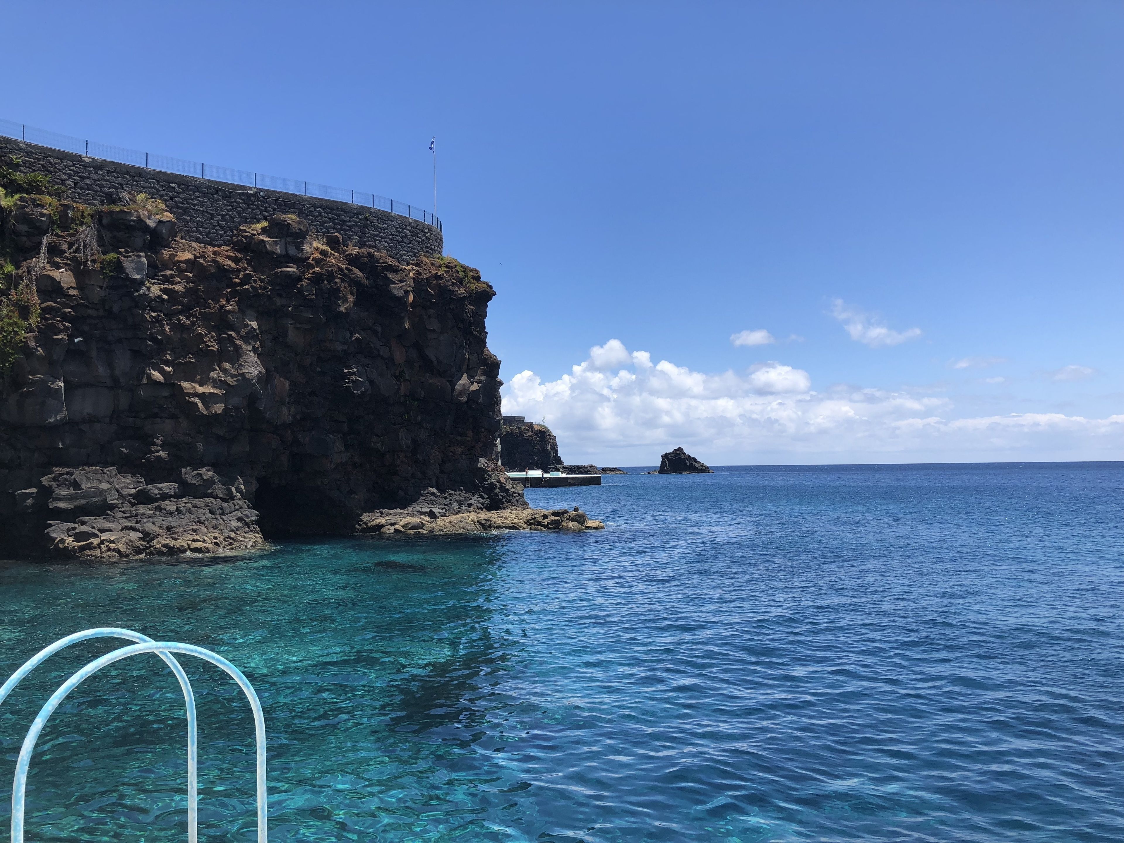 Un paysage côtier avec une eau bleue et limpide, des falaises rocheuses et une île lointaine.