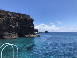 Cena costeira com águas azul-claras, falésias rochosas e uma ilha ao longe.