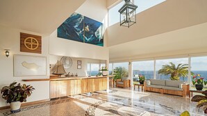 A spacious lobby with a reception desk, large windows offering ocean views, and a high ceiling with a hanging lantern.