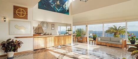 A spacious lobby with a reception desk, large windows offering ocean views, and a high ceiling with a hanging lantern.