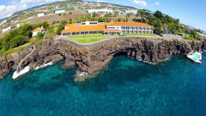 A coastal property with a large building, a rocky shoreline, and clear blue waters.