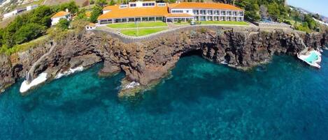A coastal property with a large building, a rocky shoreline, and clear blue waters.