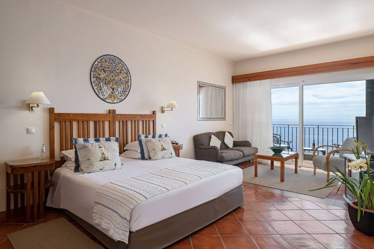 Une chambre d’hôtel avec un grand lit, un canapé, une table à manger et un balcon donnant sur la mer.