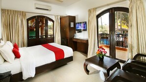 A hotel room with a bed, a desk, a TV, and a balcony with curtains. - Calangute Grande (Calangute)