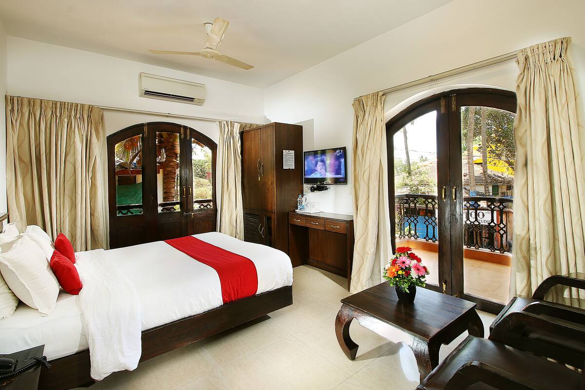 A hotel room with a bed, a desk, a TV, and a balcony with curtains.