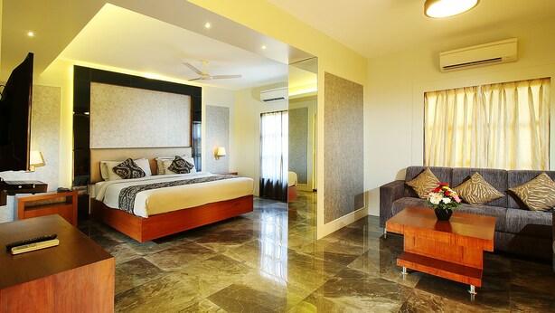 A modern hotel room with a large bed, a sofa, a coffee table, and a TV. - Calangute Grande (Calangute)