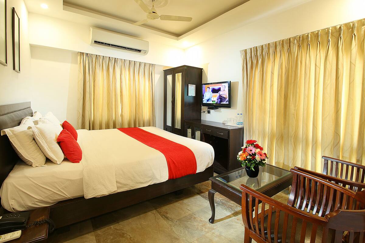 A hotel room with a large bed, a desk with a TV, and a glass table with chairs.