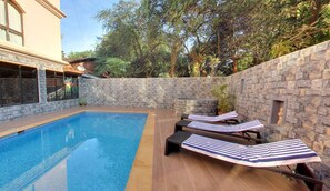 A swimming pool with lounge chairs and a stone wall. - Calangute Grande (Calangute)