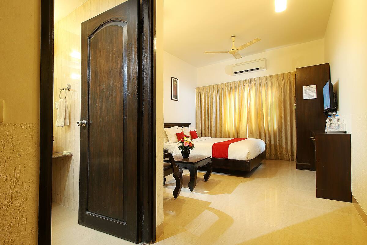A hotel room with a bed, a desk, a chair, a television, and a ceiling fan.