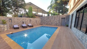 A swimming pool with lounge chairs and a stone wall. - Calangute Grande (Calangute)