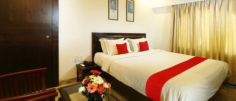 A hotel room with a large bed, a wooden chair, a nightstand, and a vase of flowers.