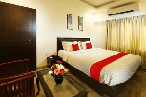 A hotel room with a large bed, a wooden chair, a nightstand, and a vase of flowers.