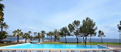 A pool area with lounge chairs and a view of the sea.