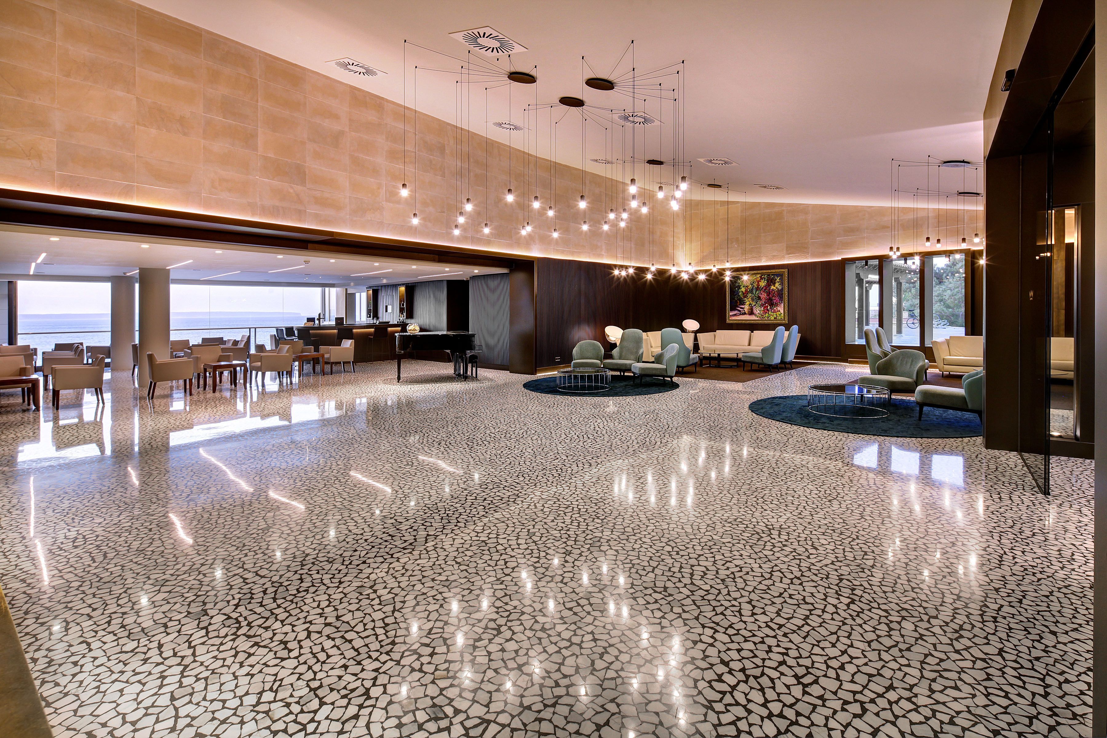 A spacious lobby with a polished tile floor, seating areas, and a view of the sea.