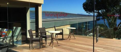 En moderne udendørs terrasse med glasgelændere, trægulv og siddeområder.
