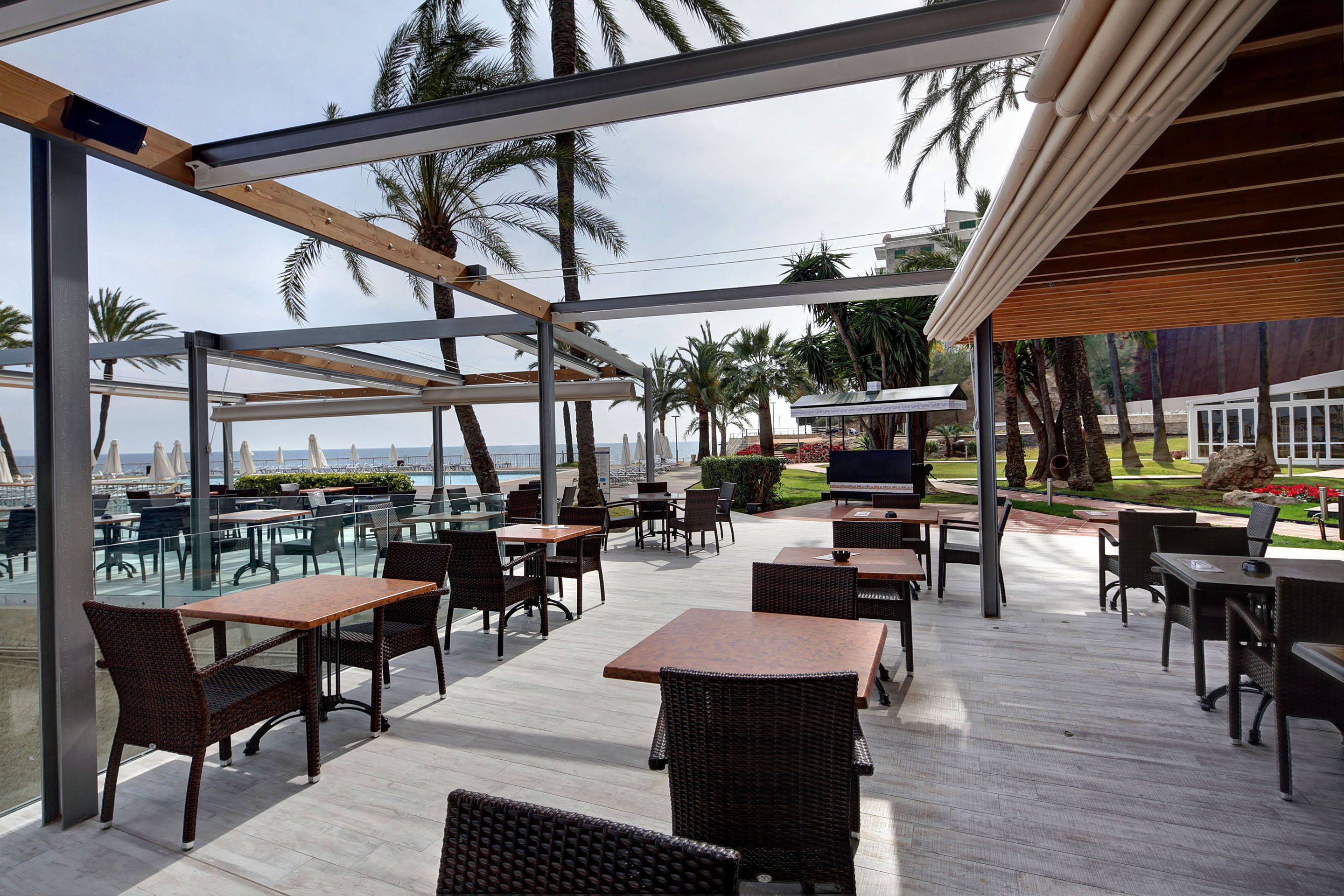 Un espace de restauration en plein air, avec des tables et des chaises, offrant une vue panoramique sur un paysage agrémenté de palmiers et d’une étendue d’eau.