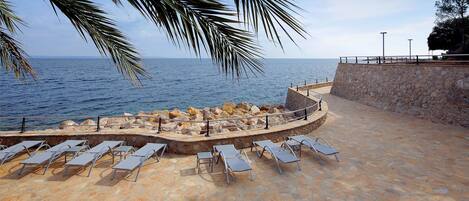 A stone deck with sun loungers overlooking the sea.