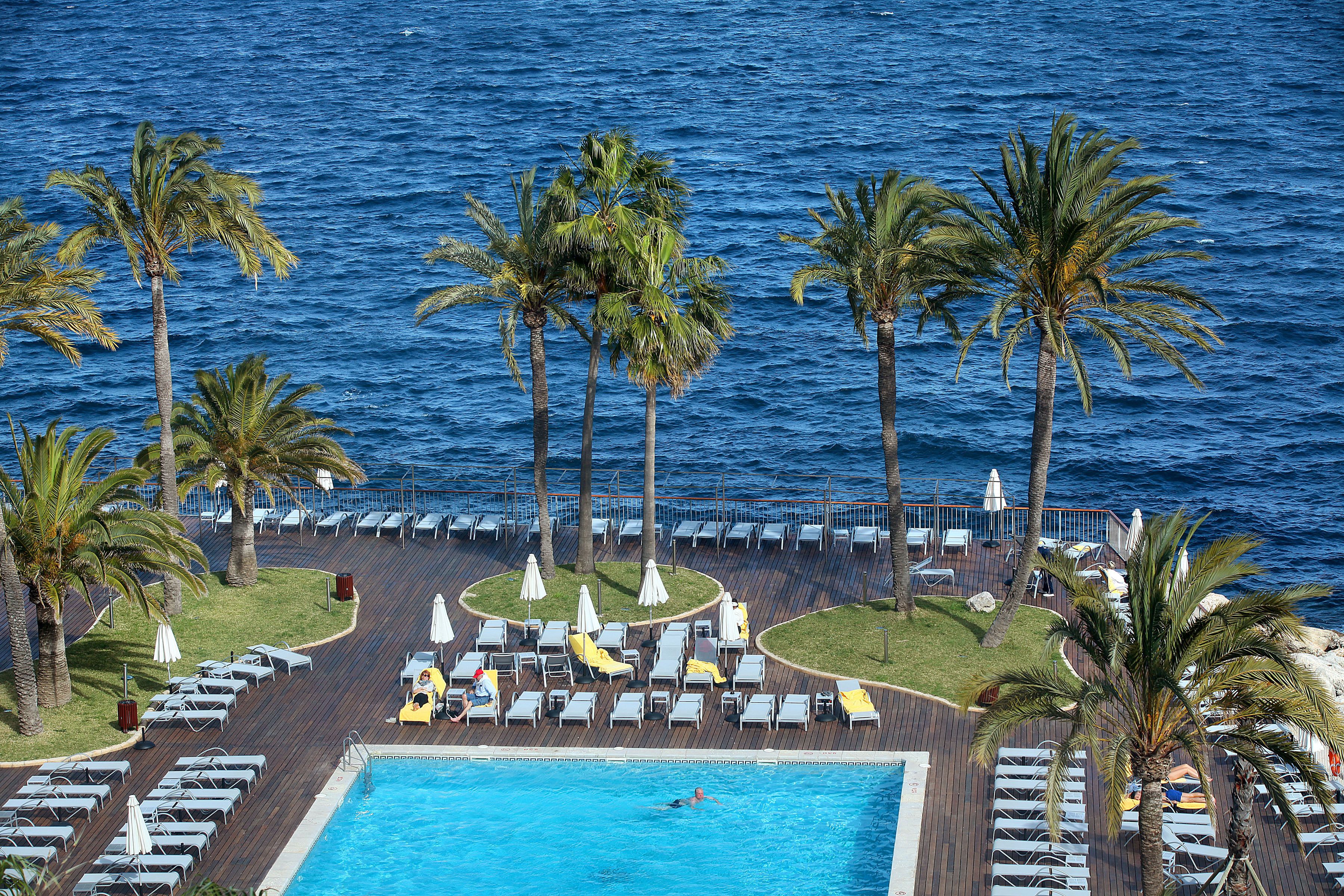 Zona de piscina en un complejo turístico con tumbonas, palmeras y vistas al océano.