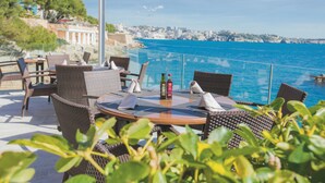 An outdoor dining area with wicker furniture and a view of the sea.