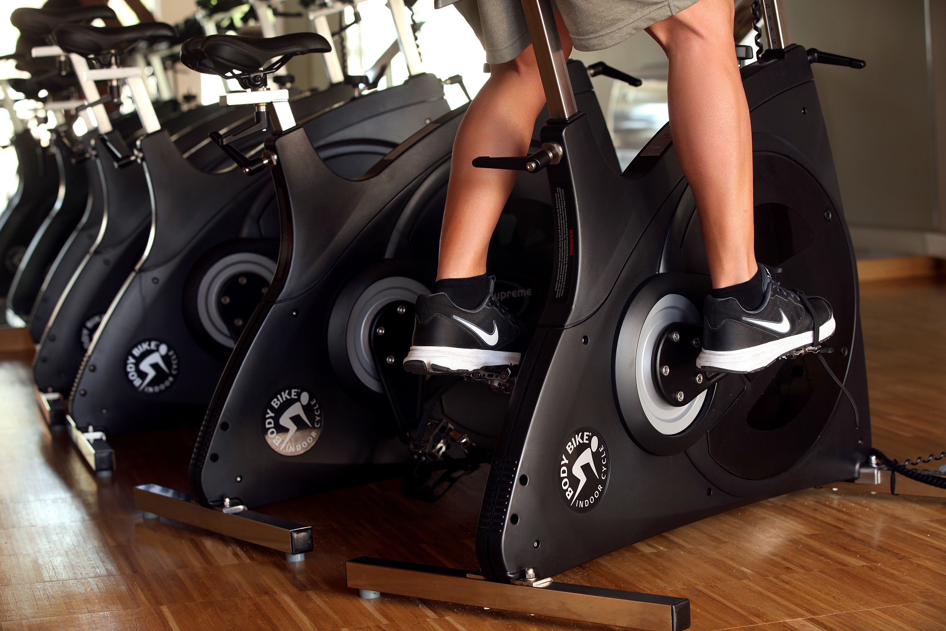 A row of stationary bikes in a gym with a wooden floor.