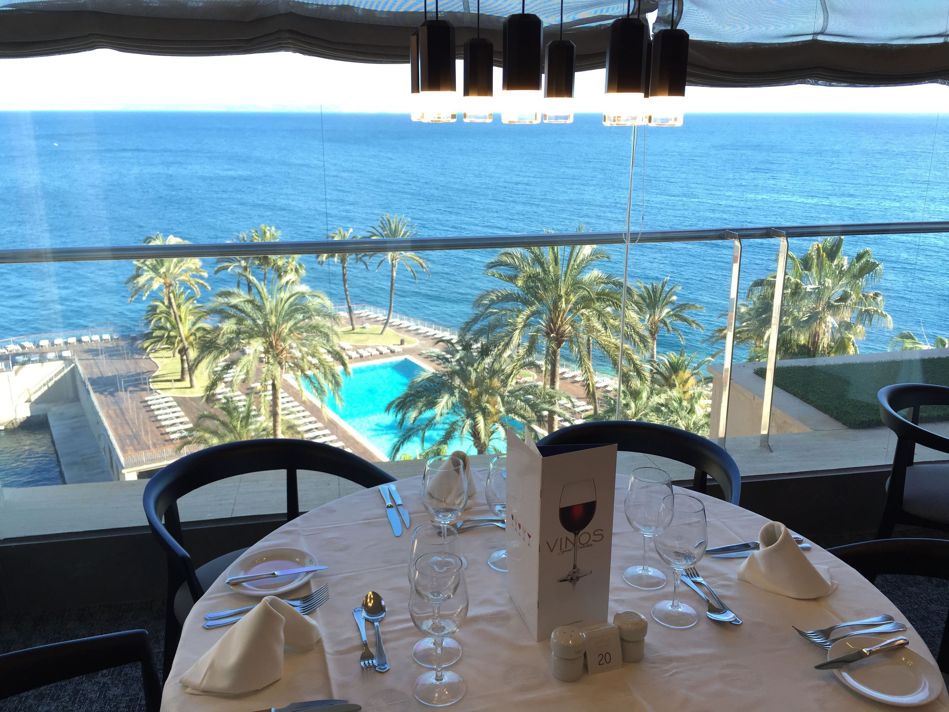 A table set for dining with a view of the ocean and a pool.
