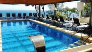 Una piscina con sillas de descanso y vista al océano.
