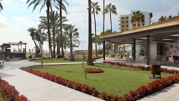 A modern outdoor area with a pathway, palm trees, and a building with outdoor seating.
