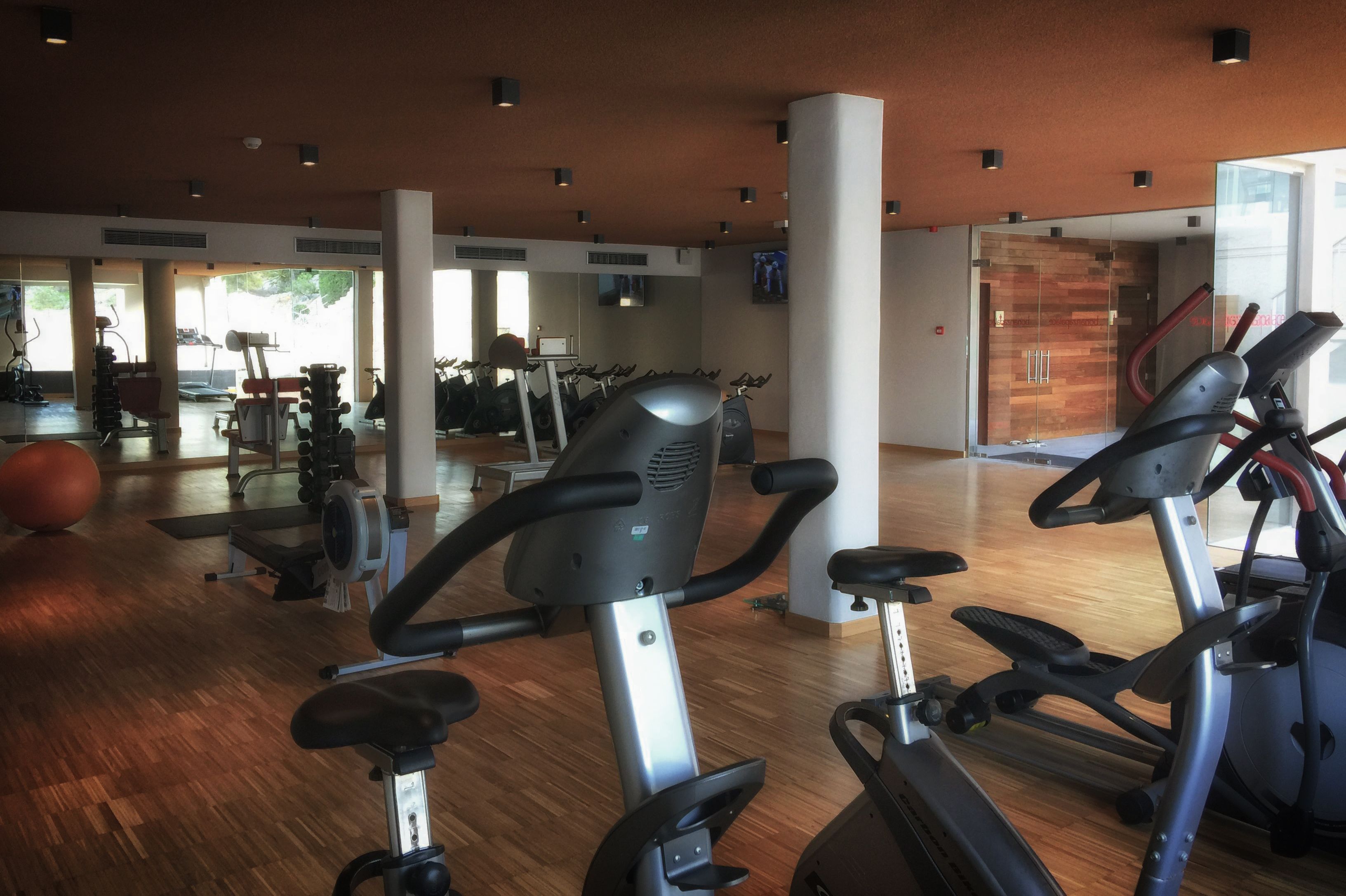 A gym with exercise equipment, wooden flooring, and large windows.