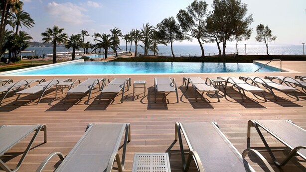 A poolside area with sun loungers and a view of the sea.