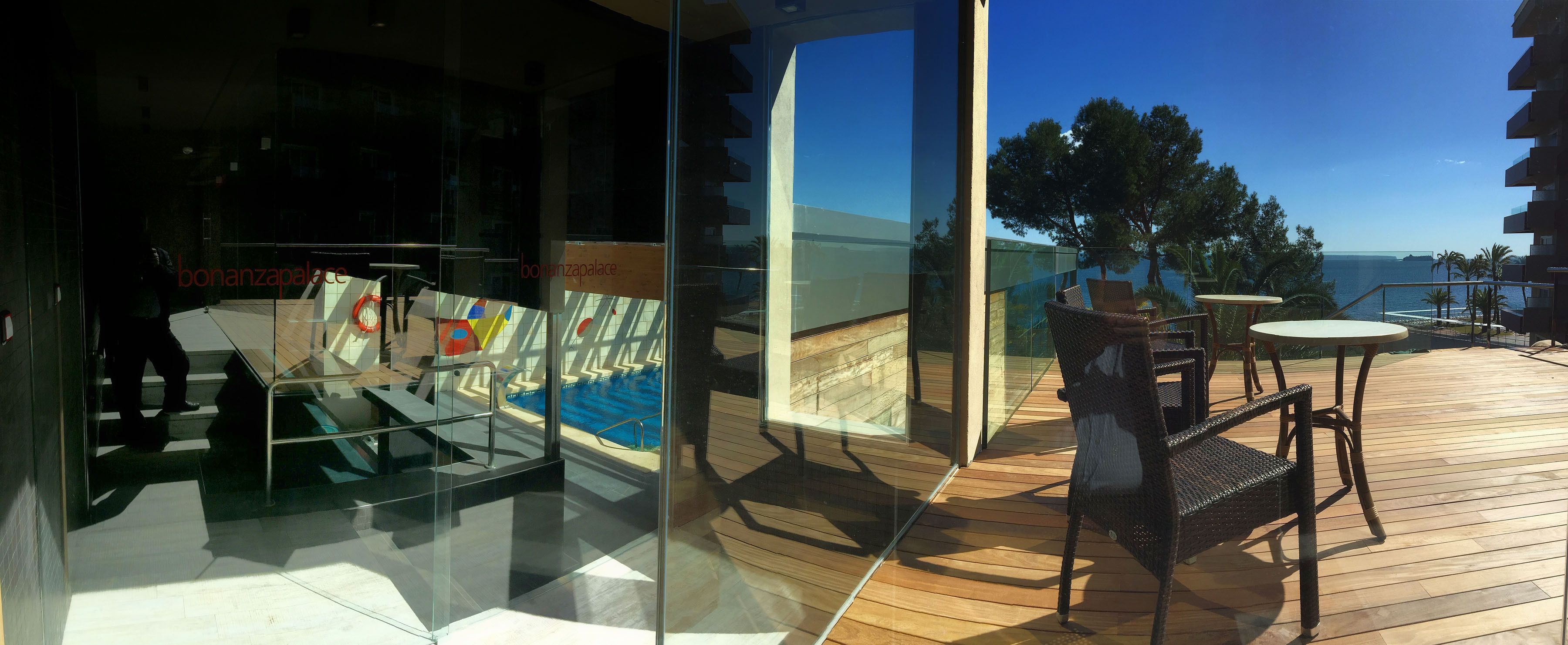 Un espacio con paredes de vidrio, una terraza de madera, mobiliario exterior y vista al mar.