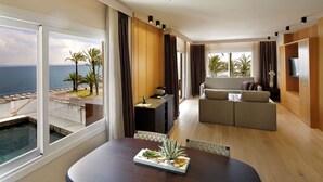 A modern living room with a large window overlooking a pool and the sea, a sofa, a dining table with a plant centerpiece, and wooden paneling.