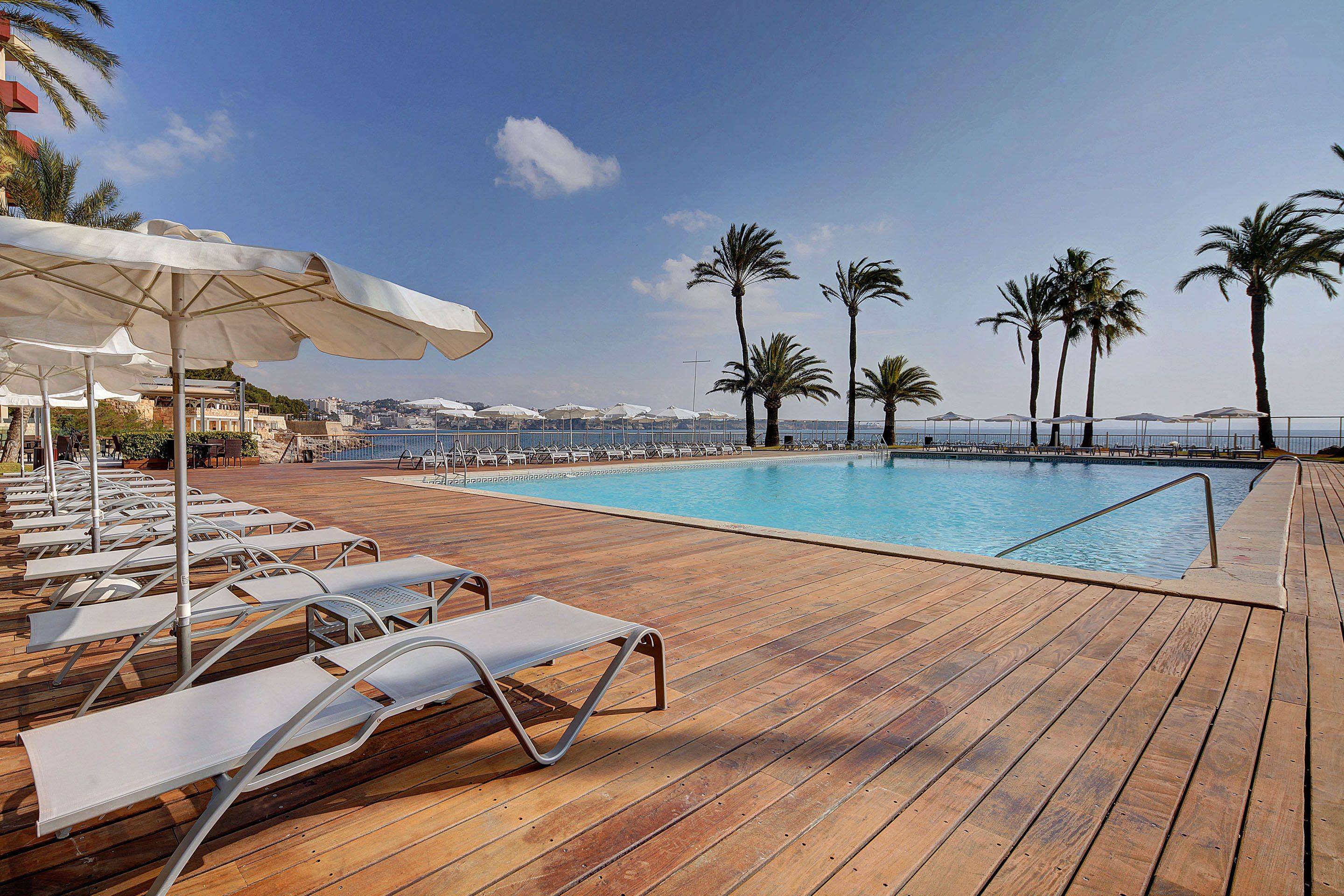 A wooden deck with lounge chairs and umbrellas overlooking a pool.