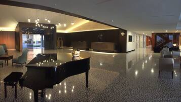 A spacious lobby with a grand piano, modern seating, and a sleek, polished floor.