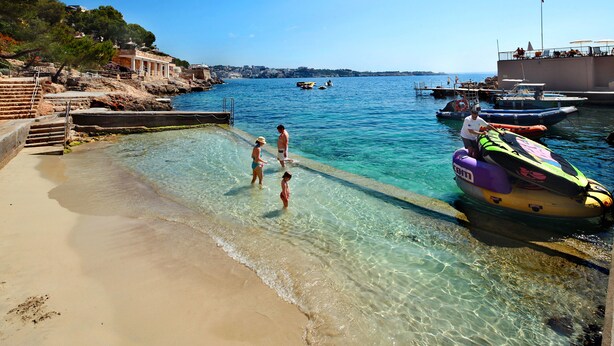A clear waterfront with a sandy beach and a jet ski docked on the right.