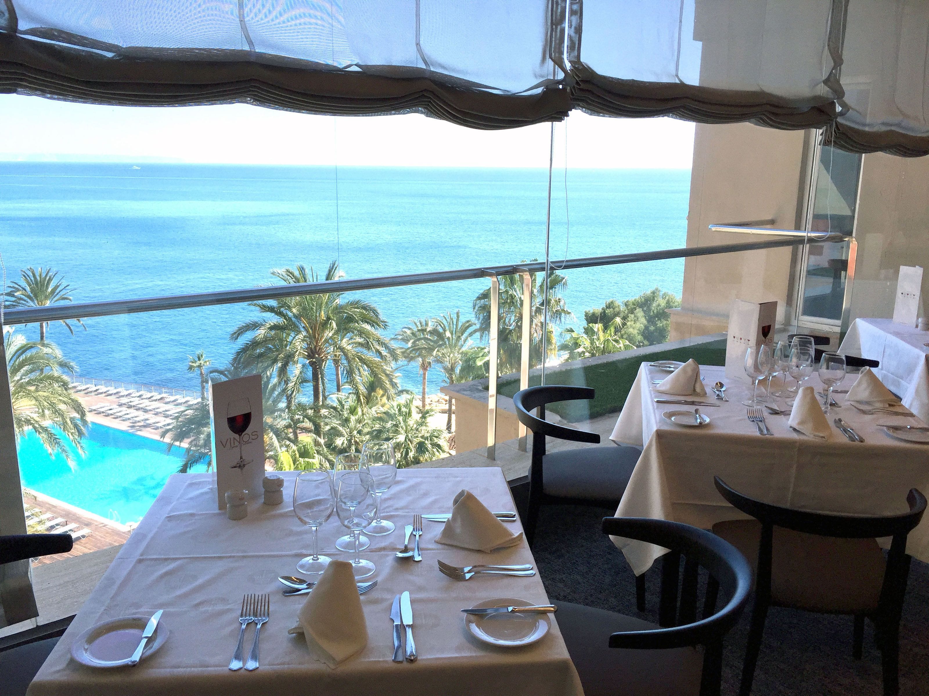 A dining table set for two with a view of the ocean and palm trees.