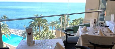 A dining table set for two with a view of the ocean and palm trees.