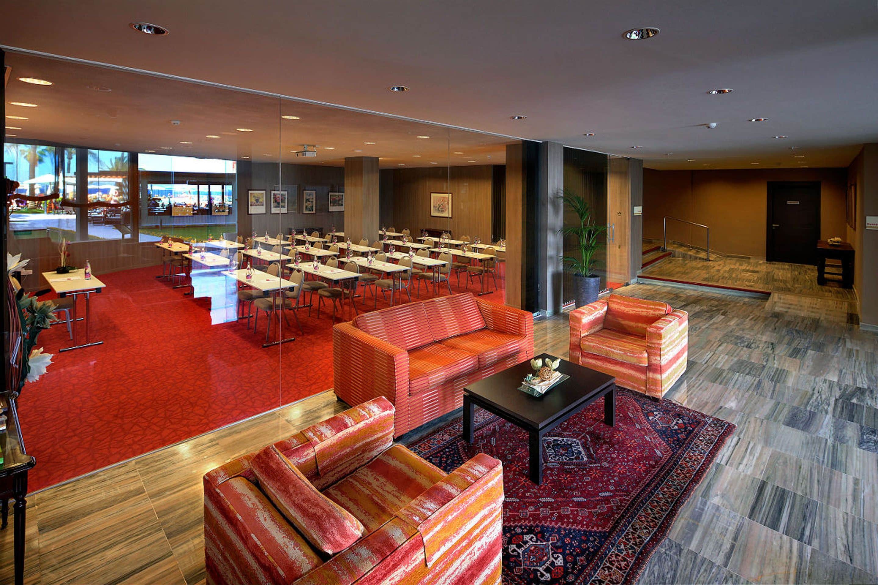 Un vestíbulo de hotel con alfombra roja, varias zonas de estar y vistas al exterior.