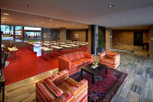 Un vestíbulo de hotel con alfombra roja, varias zonas de estar y vistas al exterior.