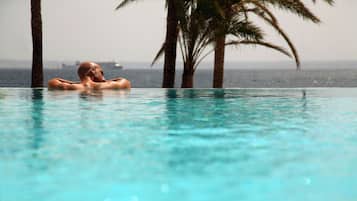 Una persona relajándose en una piscina azul cristalina, con palmeras al fondo.