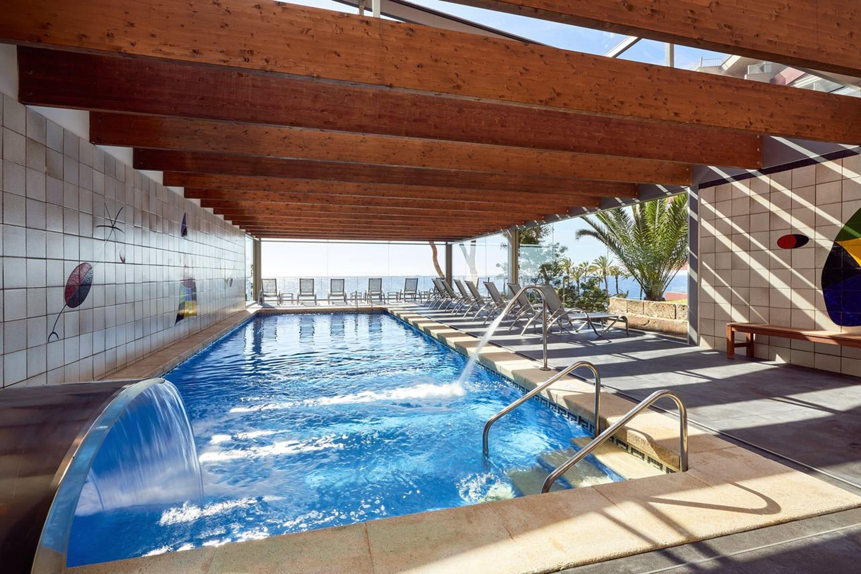 A swimming pool with a wooden ceiling, tiled walls, and a bench.