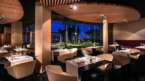 A restaurant with tables set for dining, a view of the outdoors, and a modern ceiling design.