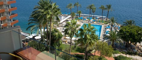 A resort with a pool, palm trees, and a view of the sea.