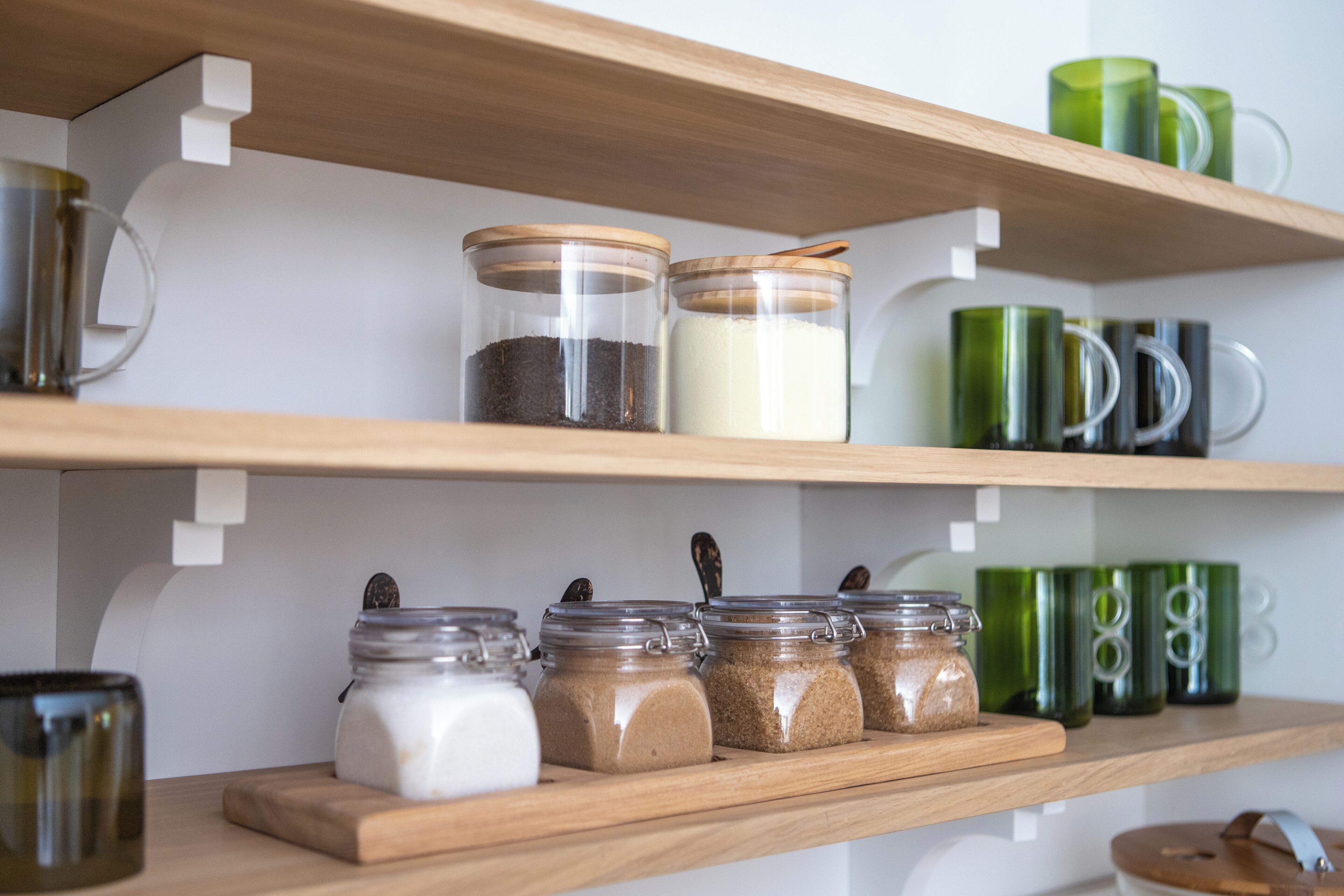 Une étagère de cuisine avec des bocaux d’épices et une tasse verte.