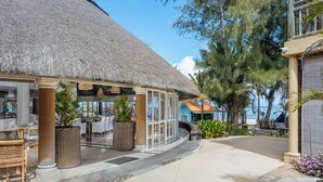 A beachfront restaurant with a thatched roof, outdoor seating, and a view of the ocean.