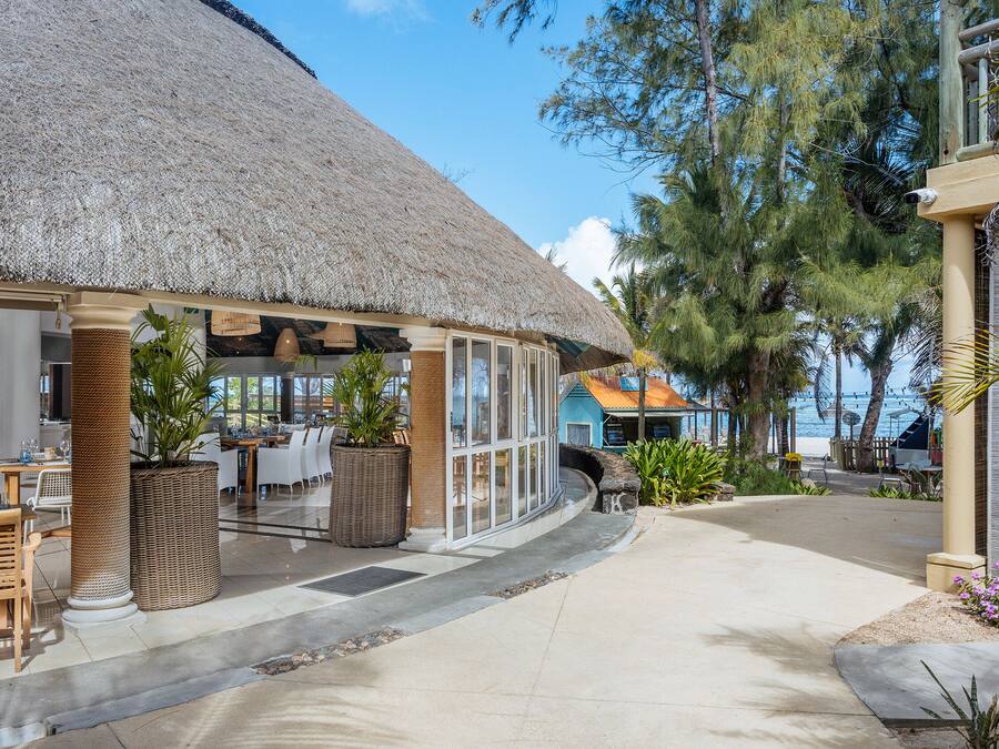 Un restaurant situé en bord de mer, doté d’un toit de chaume, de tables en plein air et offrant une vue sur l’océan.