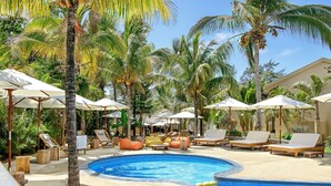 A pool area with lounge chairs and umbrellas, surrounded by palm trees.