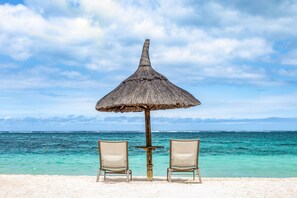 Una spiaggia con due sedie sotto un ombrellone di paglia, con vista sul mare.