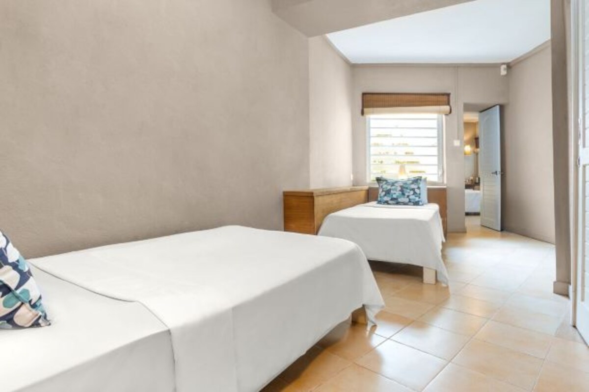 A hotel room with two single beds, a small table, and a window with a view.
